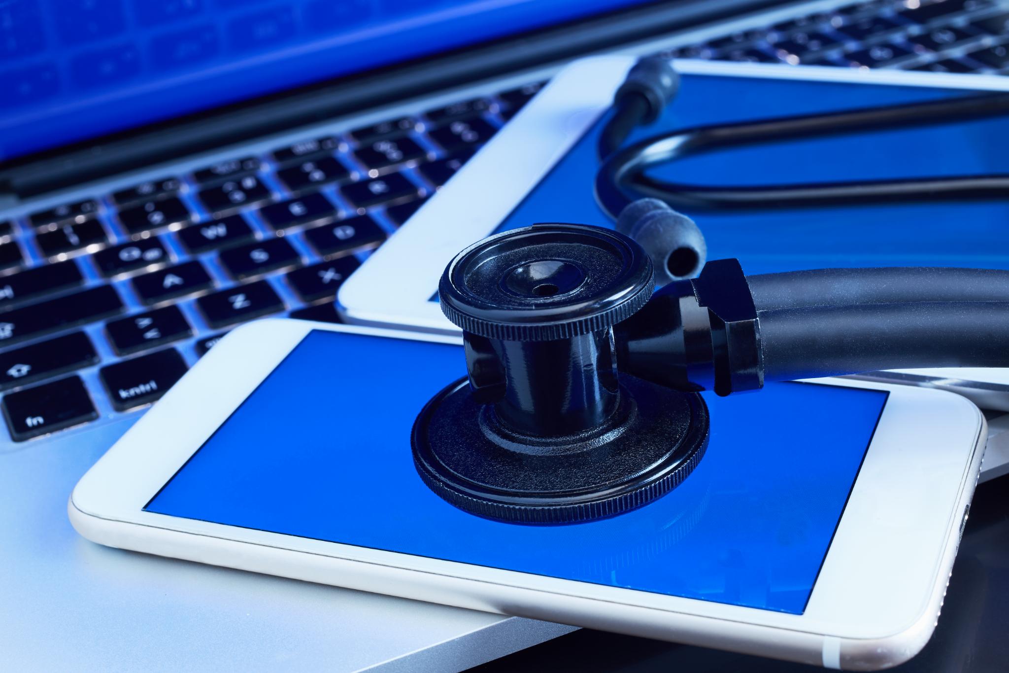 Stethoscope resting on a tablet and laptop keyboard